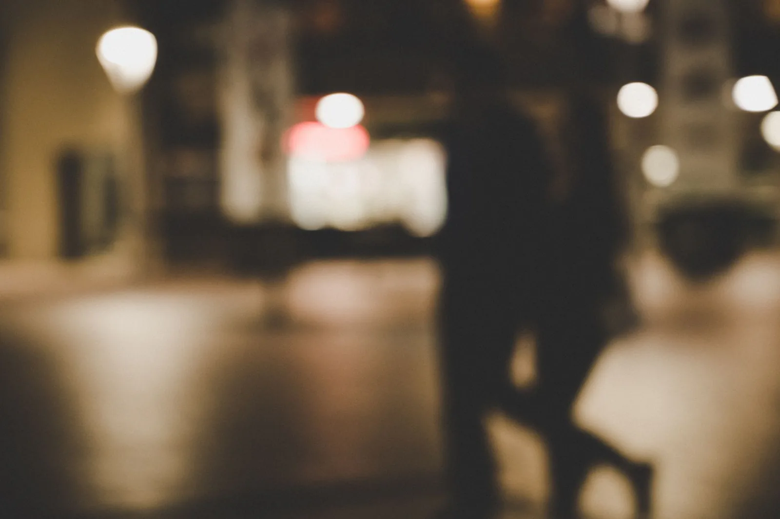 An out-of-focus couple walking at night with city lights behind them