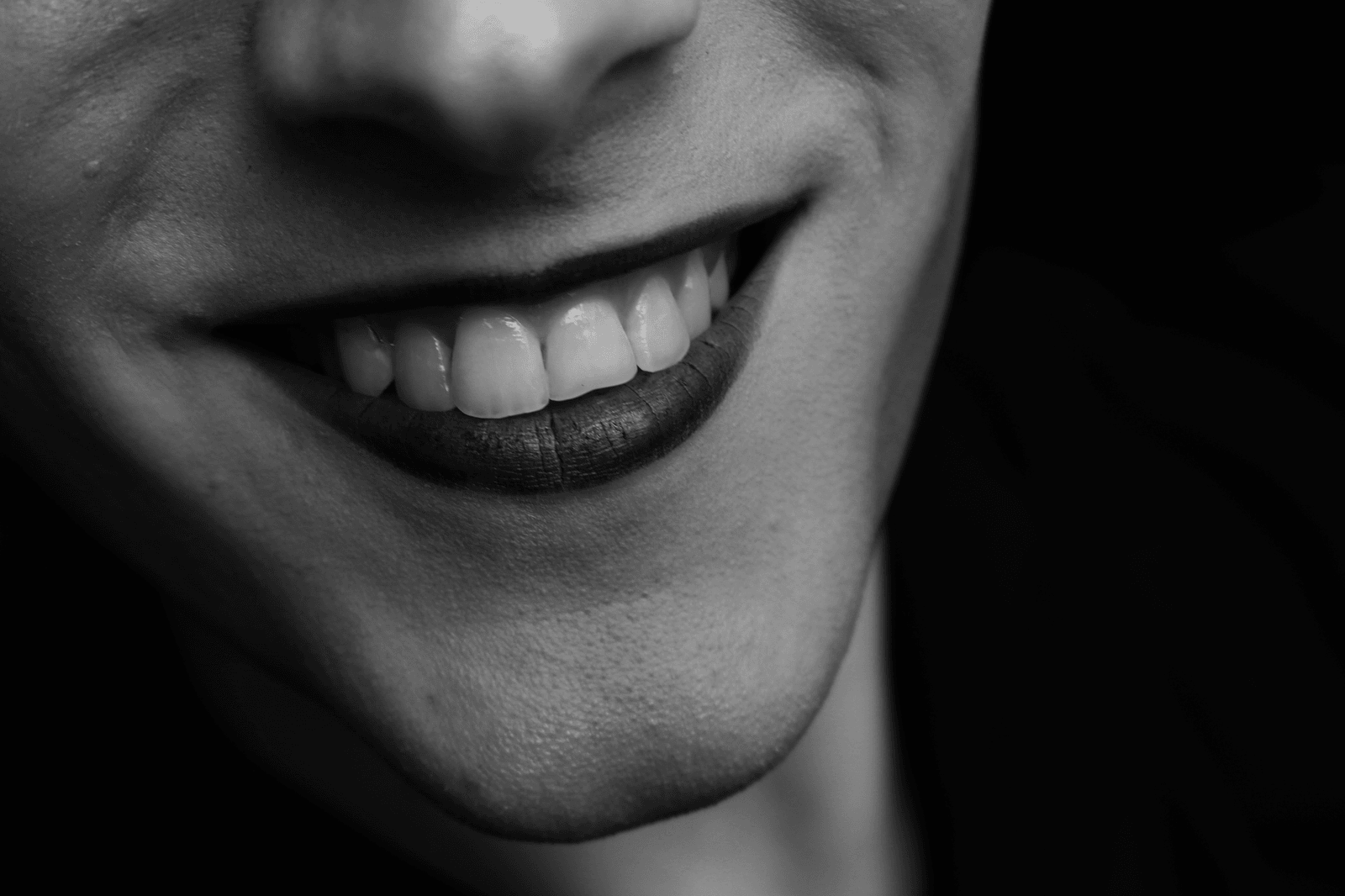 Black and white close-up of a smile with even white teeth against darkness